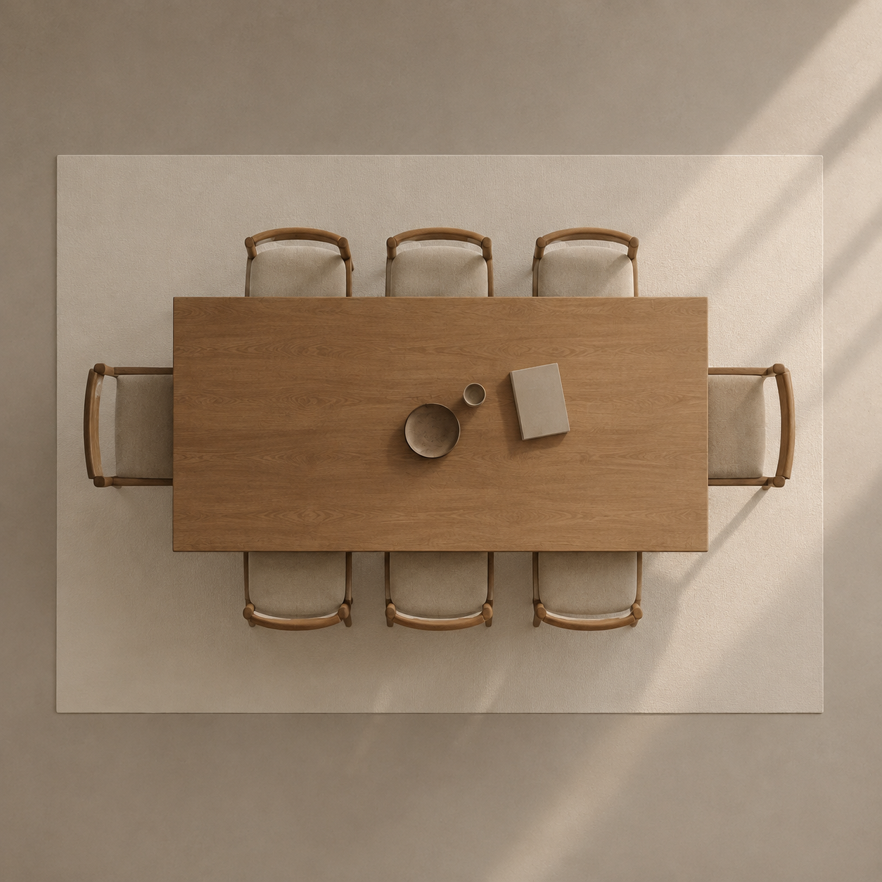 Overhead view of a rectangular wooden dining table surrounded by six matching chairs with light upholstery, placed on a large cream rug against a beige wall. A small bowl, cup, and book sit on the table.
